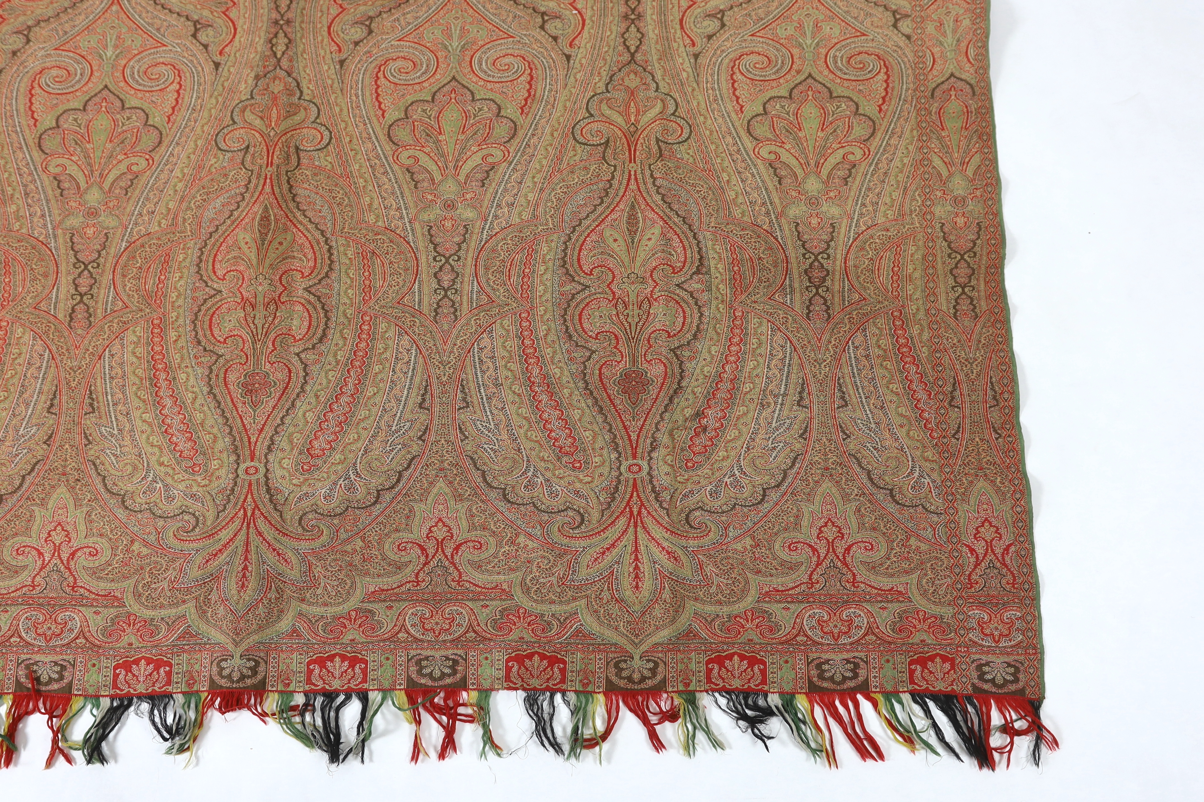 An 1860’s, reversible woven wool Paisley shawl, woven with green, red, ochre and brown, with a woven border and fringing both ends. 166cm wide x 169cm long